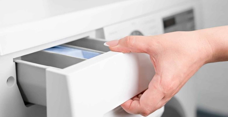 A woman's hand opens the detergent drawer in a washing machine.